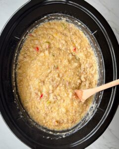 overhead shot of cooked sausage cheese grits in a black slow cooker with a wooden spoon