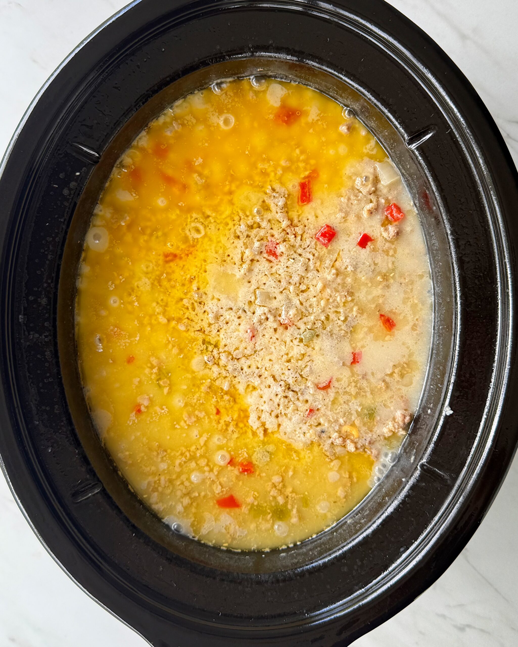 overhead shot of cooked, unstirred sausage cheese grits in a black slow cooker