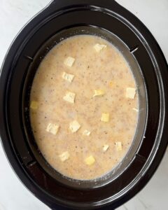 overhead shot of uncooked sausage cheese grits in a black slow cooker
