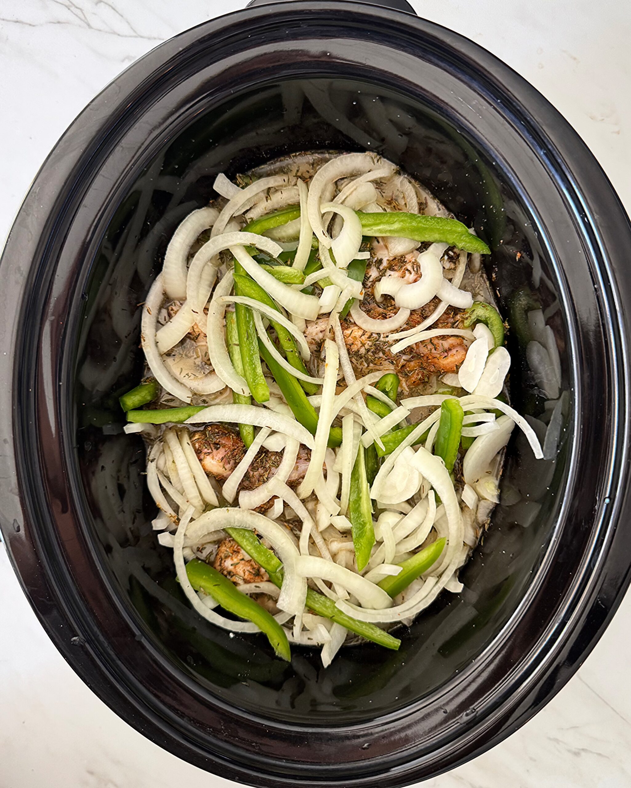 overhead shot of uncooked Smothered Turkey Wings in a black slow cooker