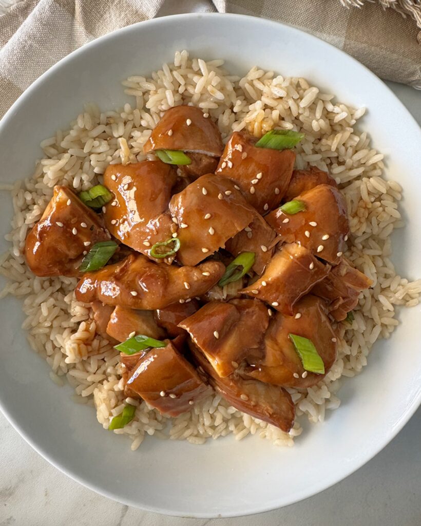overhead shot of teriyaki chicken served over white rice garnished with green onion and sesame seeds