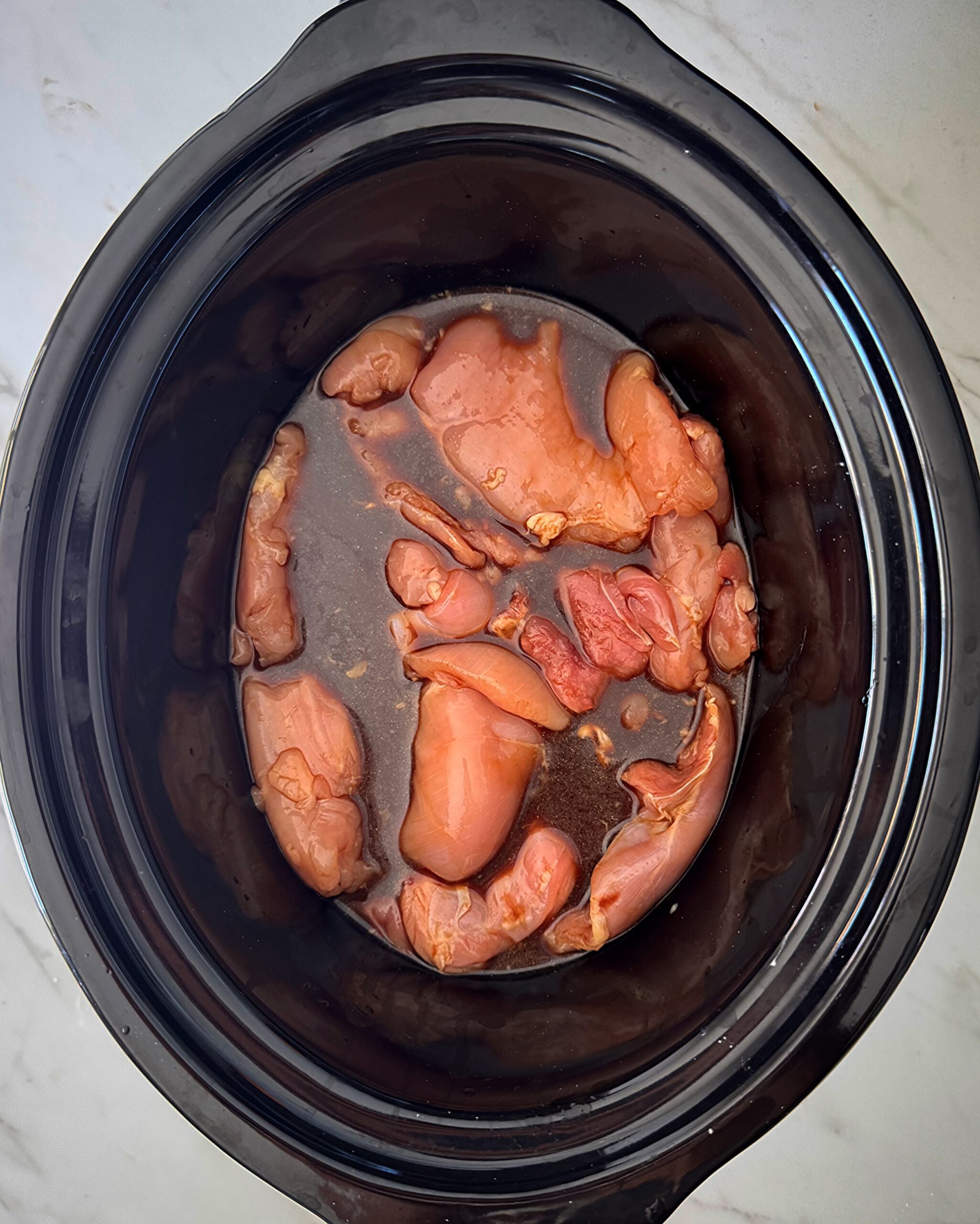 overhead shot of uncooked teriyaki chicken in a black slow cooker