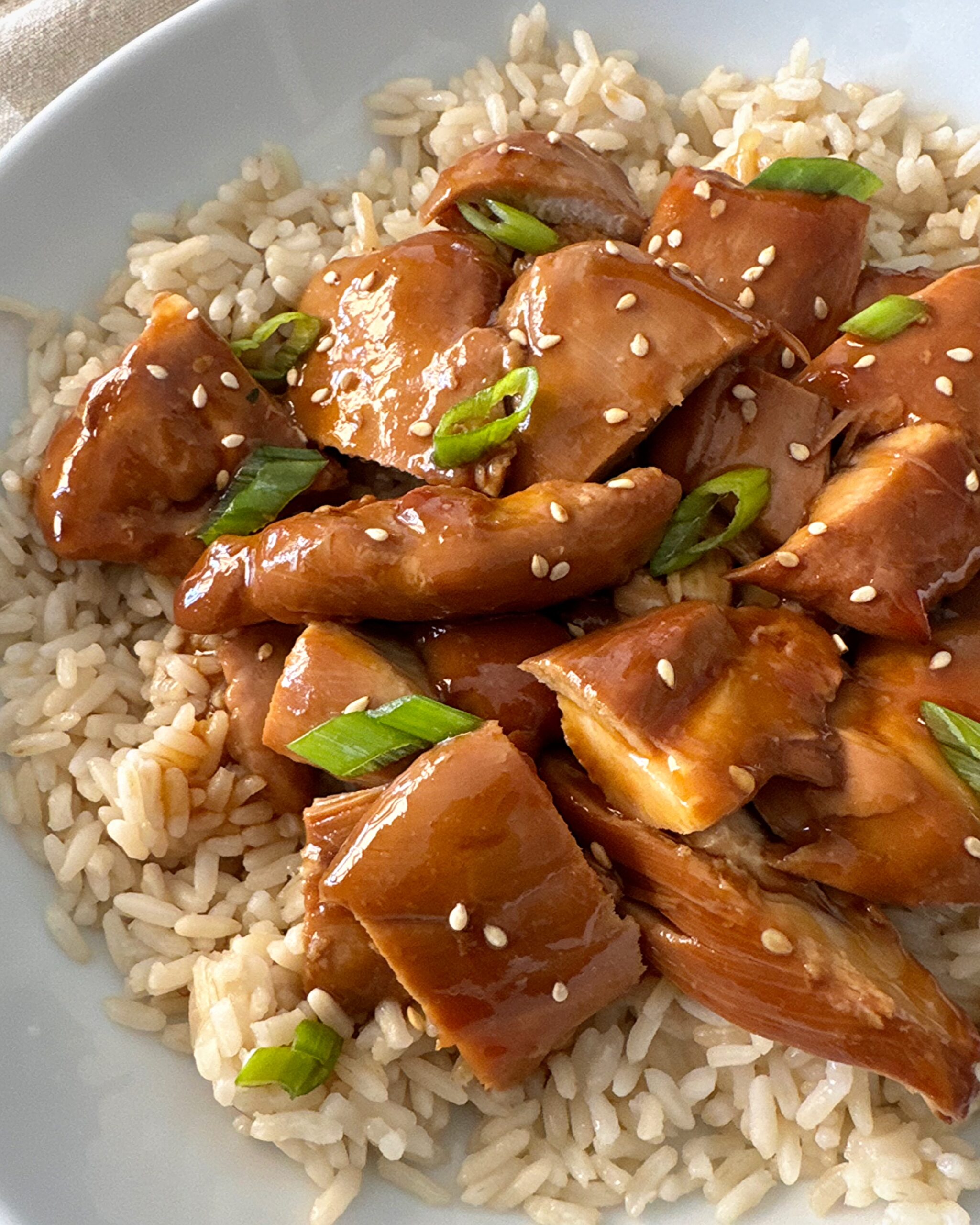 overhead shot of teriyaki chicken served over white rice garnished with green onion and sesame seeds