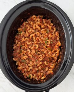 overhead shot of American Goulash in a black slow cooker garnished with fresh parsley