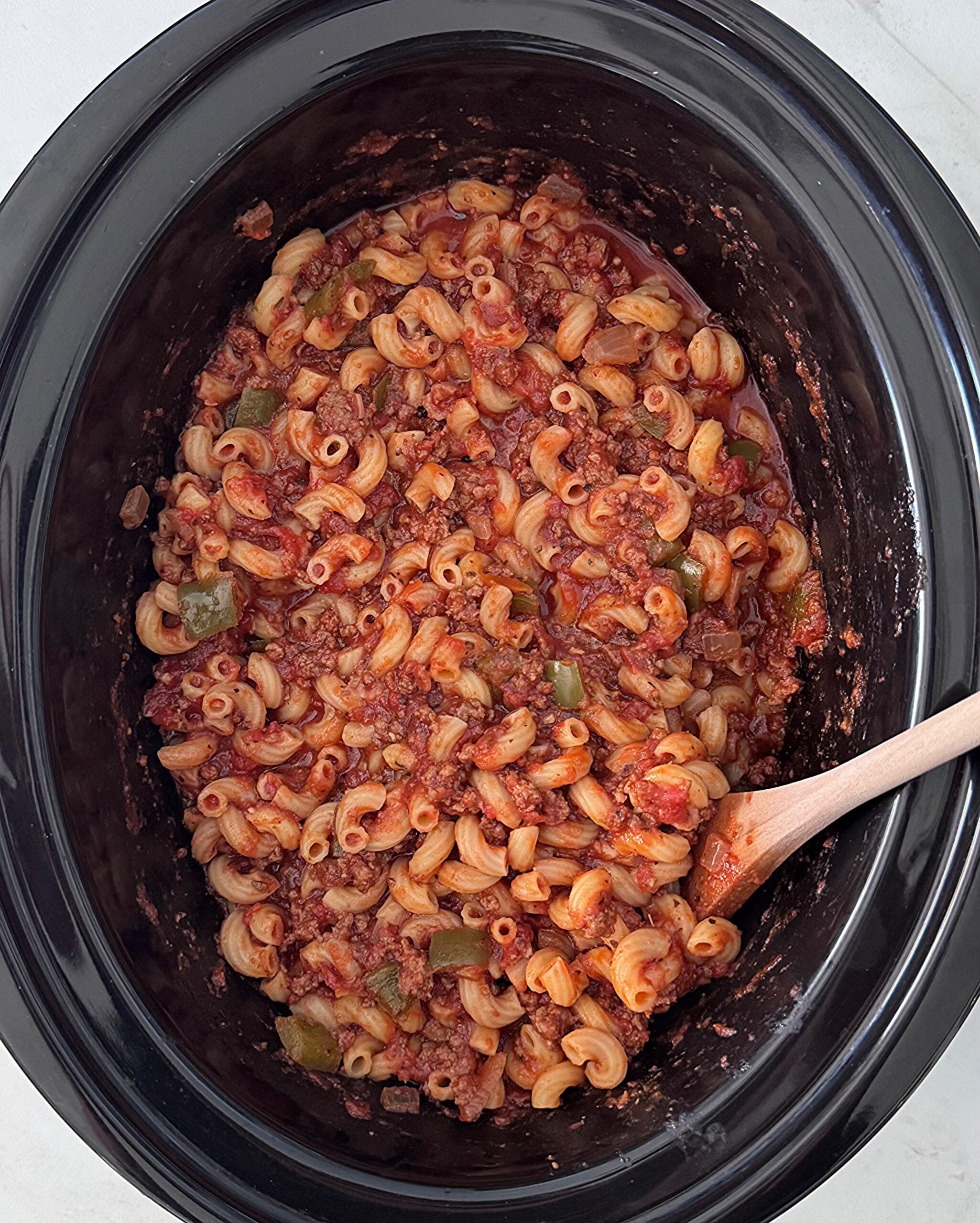 overhead shot of uncooked ingredients for American Goulash in a black slow cooker with pasta added