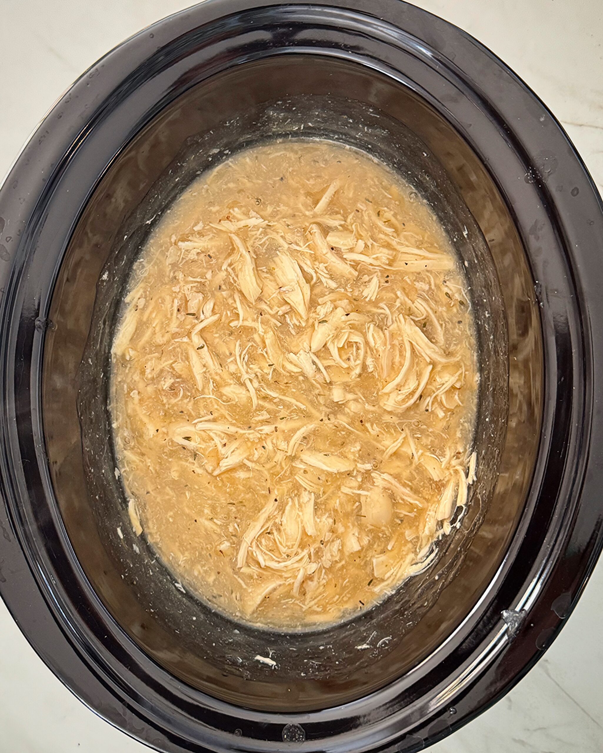 overhead shot of shredded chicken and gravy in a black slow cooker