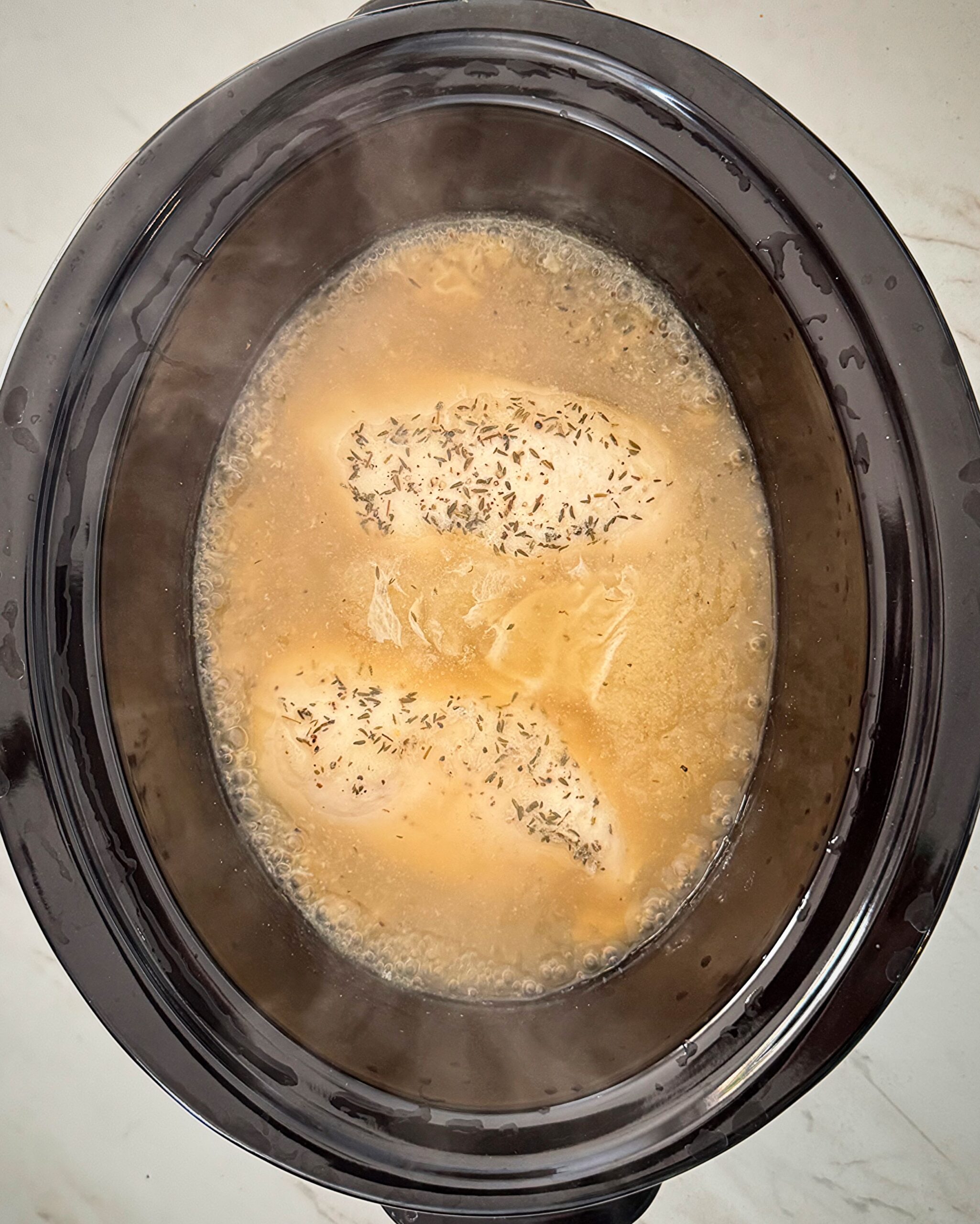 overhead shot of cooked chicken and gravy in a black slow cooker