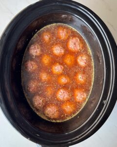 overhead shot of uncooked meatballs and gravy in a black slow cooker