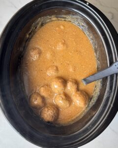 overhead shot of cooked meatballs and gravy in a black slow cooker
