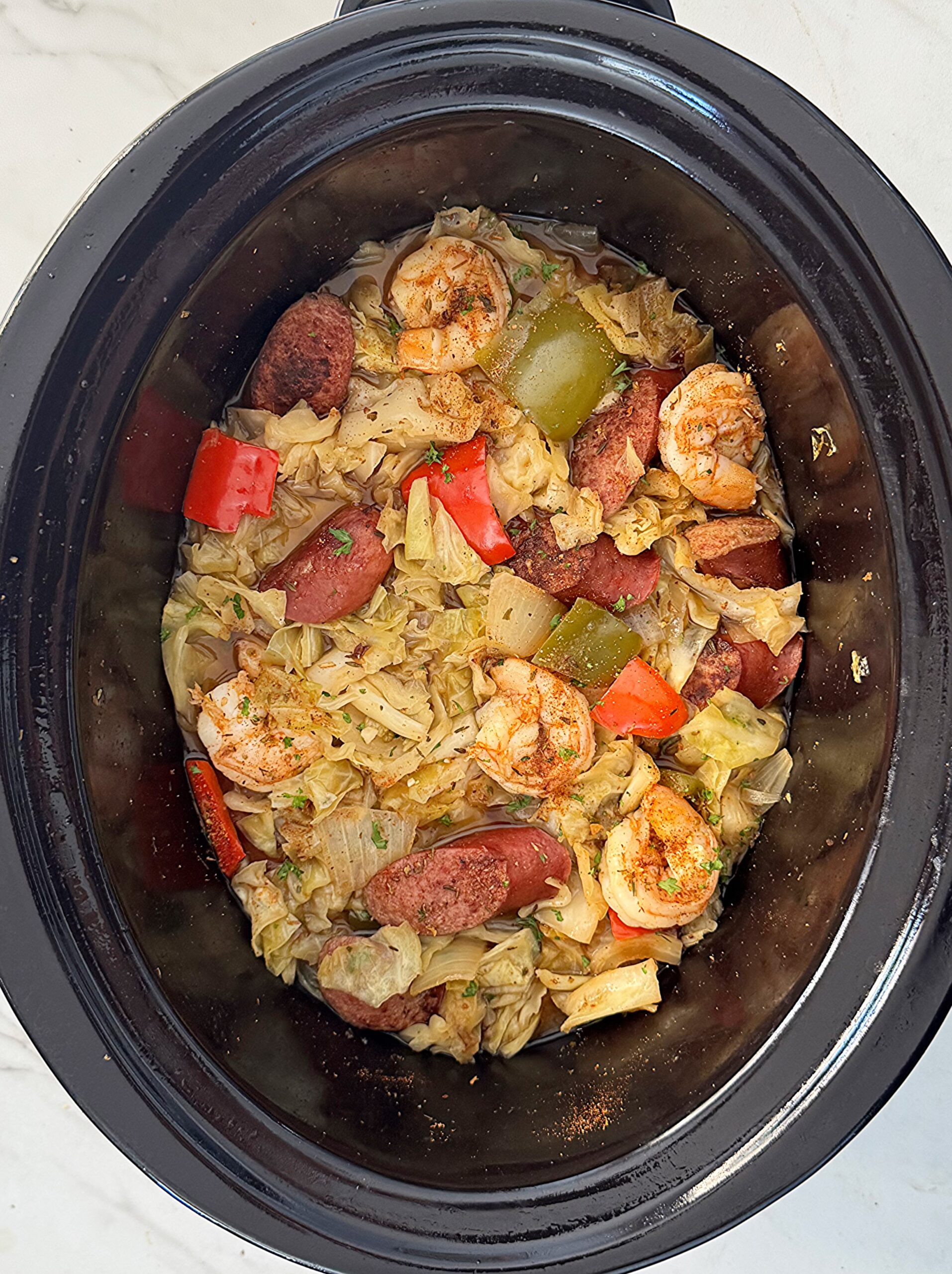 overhead shot of uncooked Cajun Cabbage Sausage Shrimp in a black slow cooker
