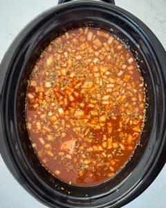 overhead shot of uncooked chicken enchilada soup in a black slow cooker
