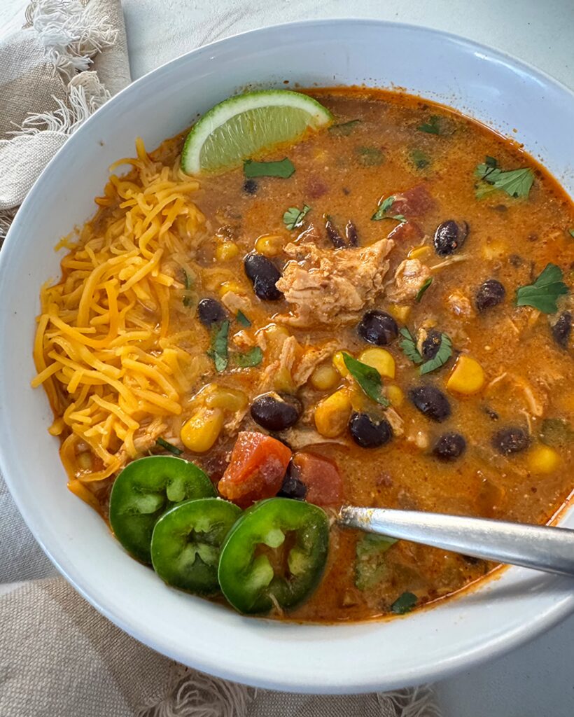 overhead shot of Crockpot Chicken Enchilada Soup in a white bowl garnished with jalapeno, cheese, and sliced lime