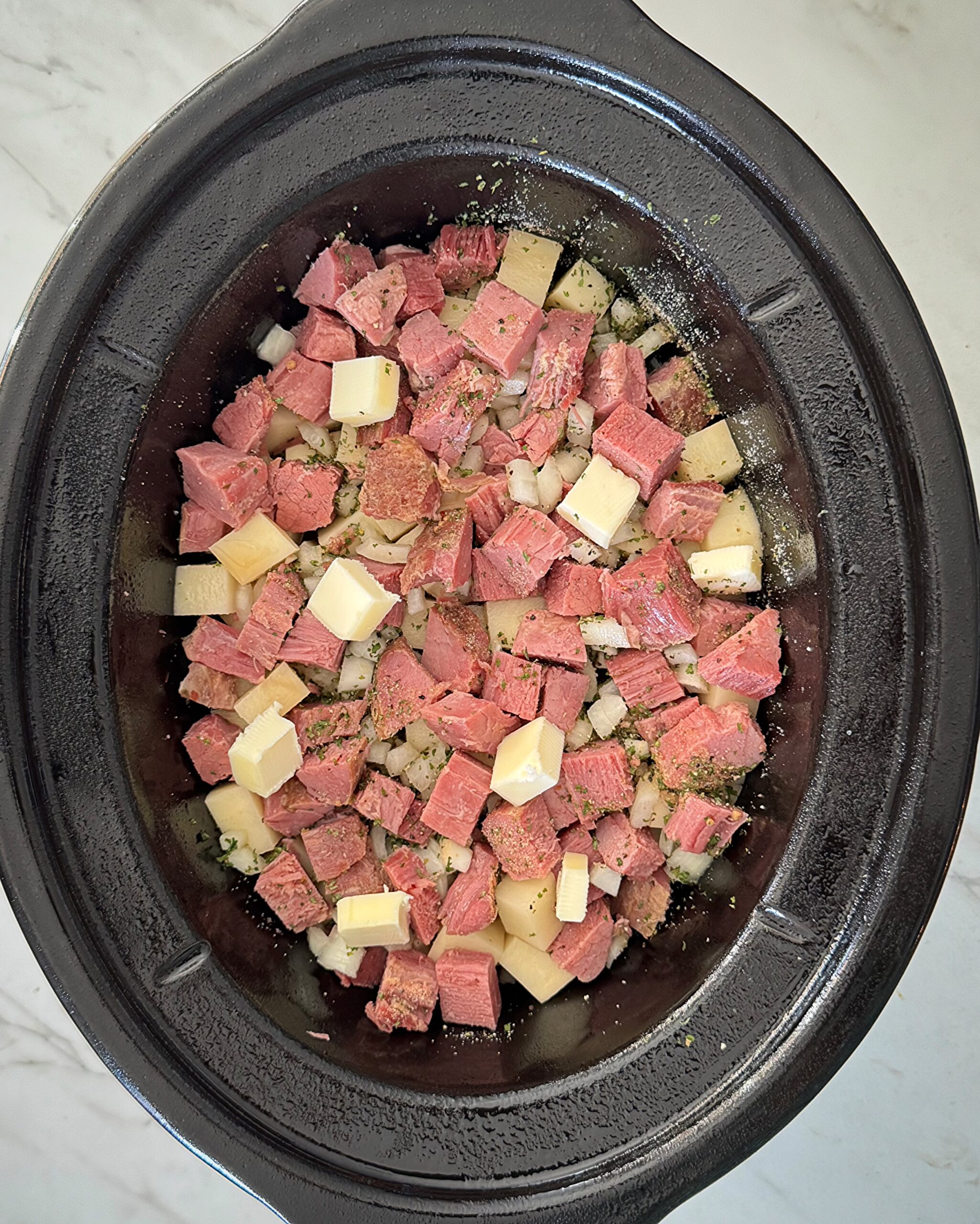 overhead shot of cooked corned beef and hash in a black slow cooker