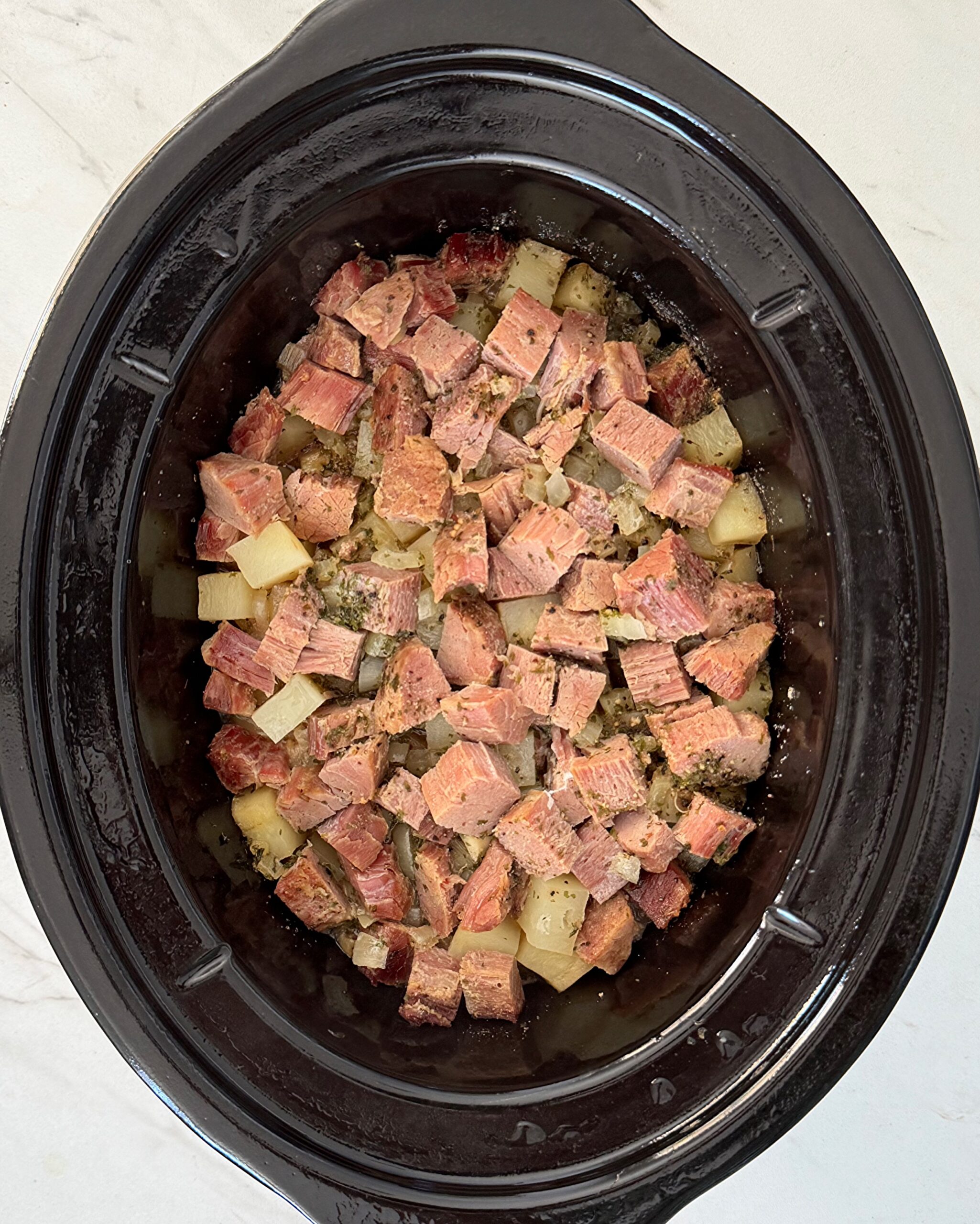overhead shot of cooked corned beef and hash in a black slow cooker