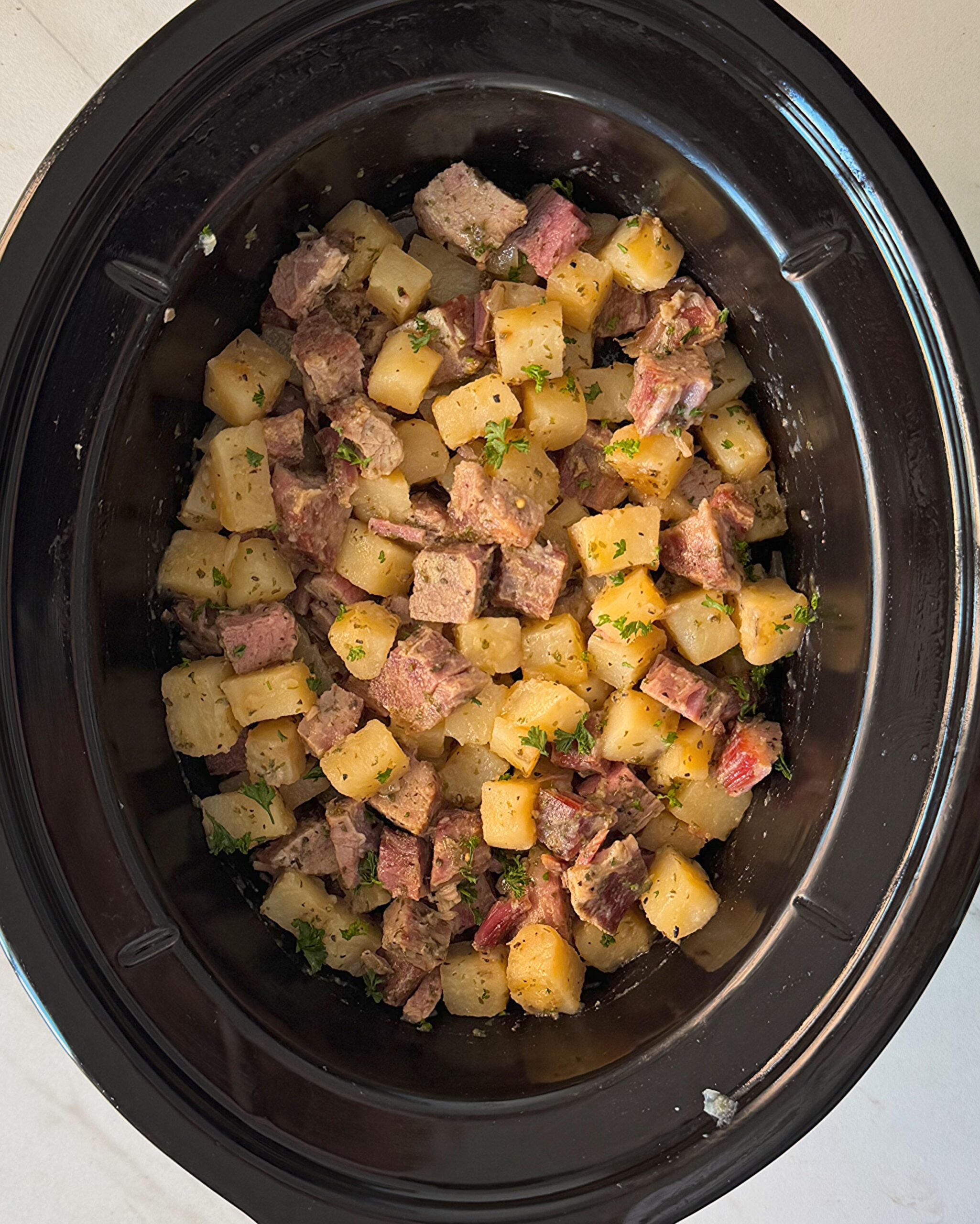 overhead shot of cooked corned beef and hash in a black slow cooker
