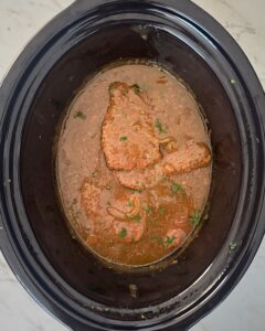 overhead shot of cooked cube steak in a black slow cooker garnished with fresh parsley