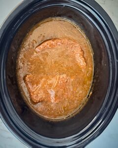 overhead shot of cooked cube steak in a black slow cooker