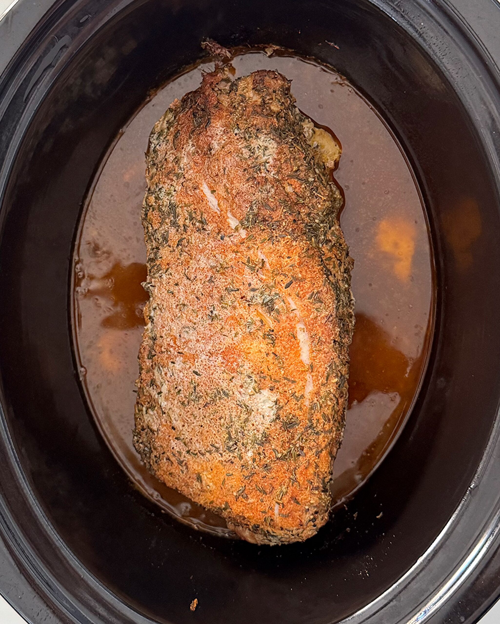 overhead shot of cooked slow cooker pork loin in a black slow cooker
