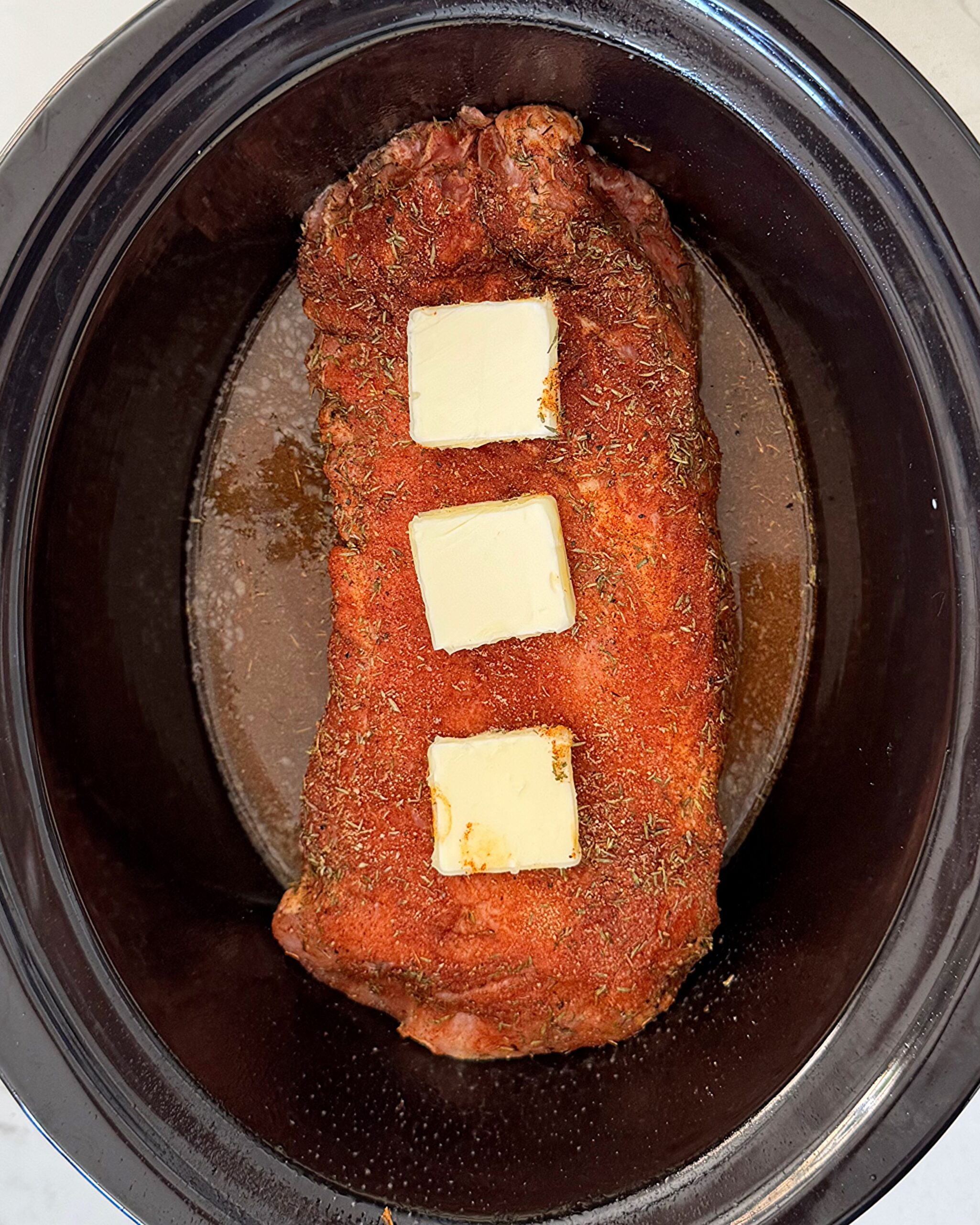 overhead shot of uncooked slow cooker pork loin in a black slow cooker