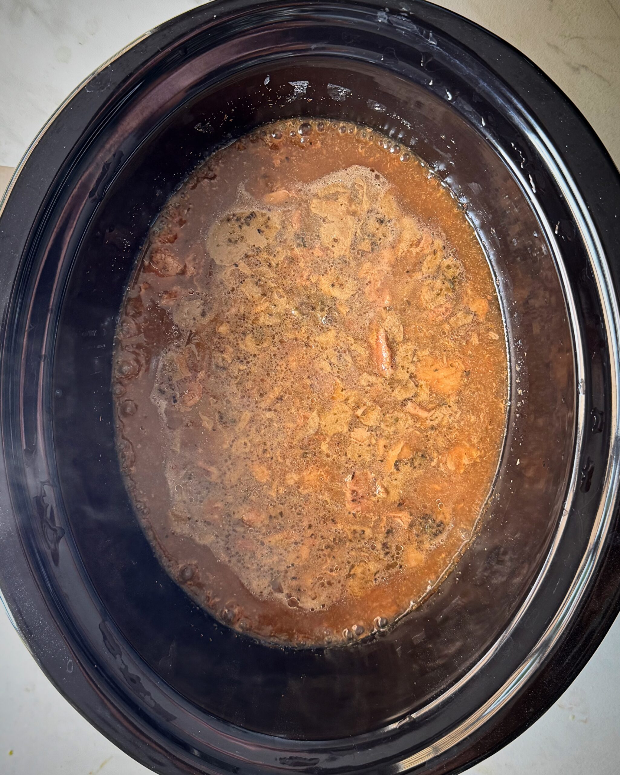 overhead shot of cooked beef tips & gravy in a black slow cooker