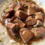 close up shot of beef tips & gravy over mashed potatoes on a white plate