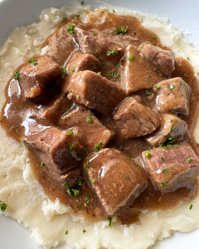 close up shot of beef tips & gravy over mashed potatoes on a white plate
