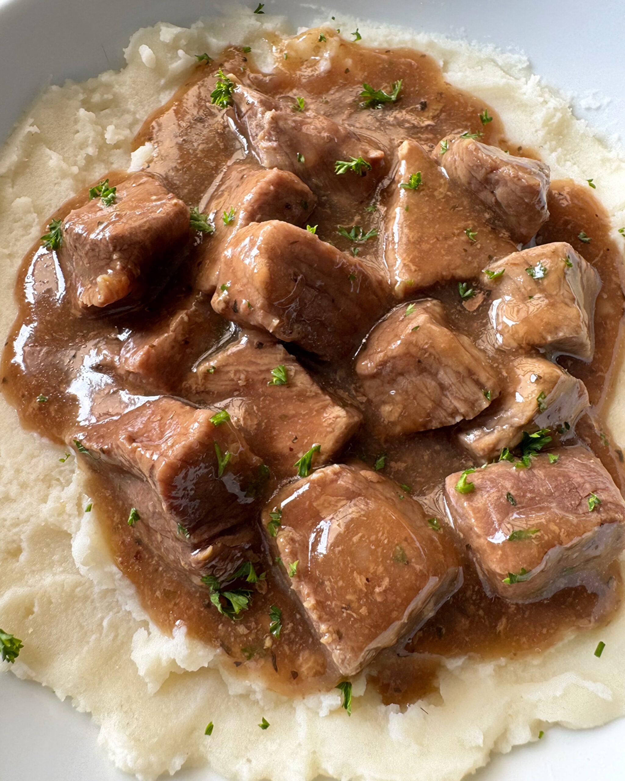 close up shot of beef tips & gravy over mashed potatoes on a white plate