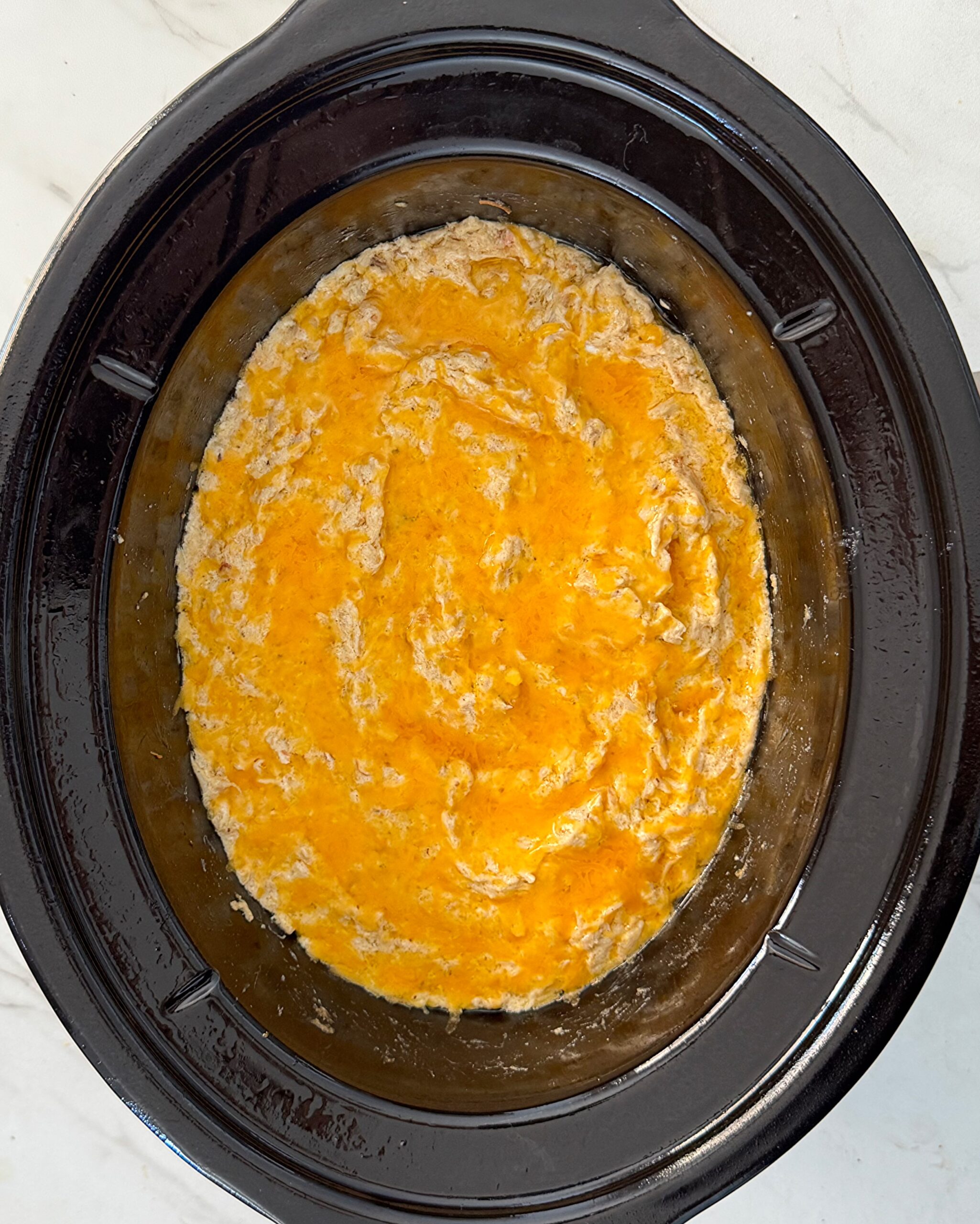 overhead shot of cooked crockpot crab dip garnished with cheese 