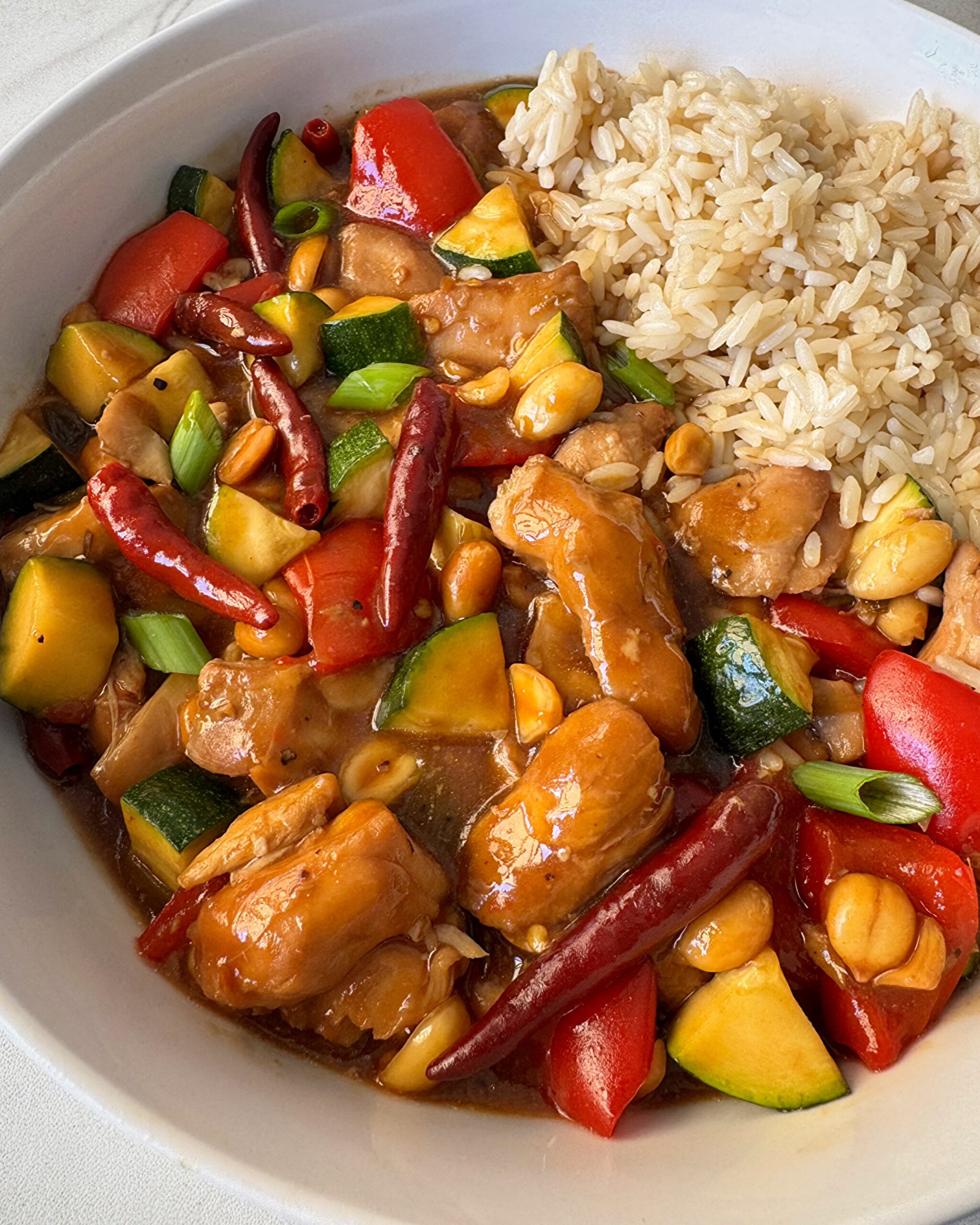 close up shot of cooked Kung Pao Chicken (Panda Express Copycat) on a white plate with white rice