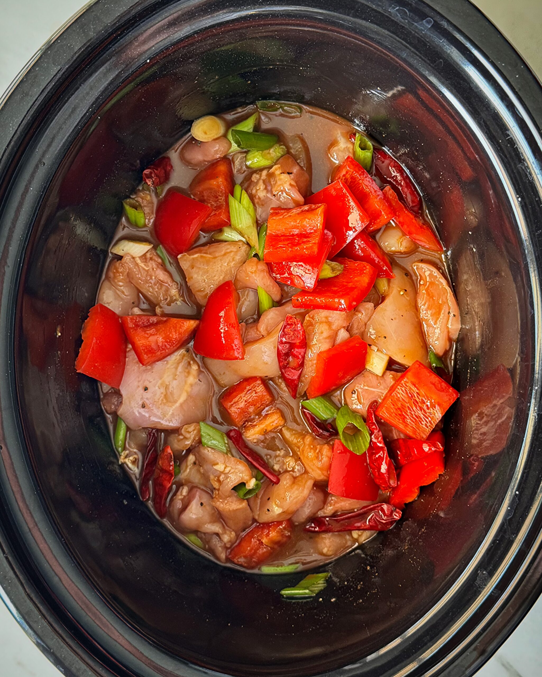 overhead shot of uncooked Kung Pao Chicken (Panda Express Copycat) in a black slow cooker