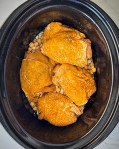 overhead shot of uncooked North African chicken in a black slow cooker