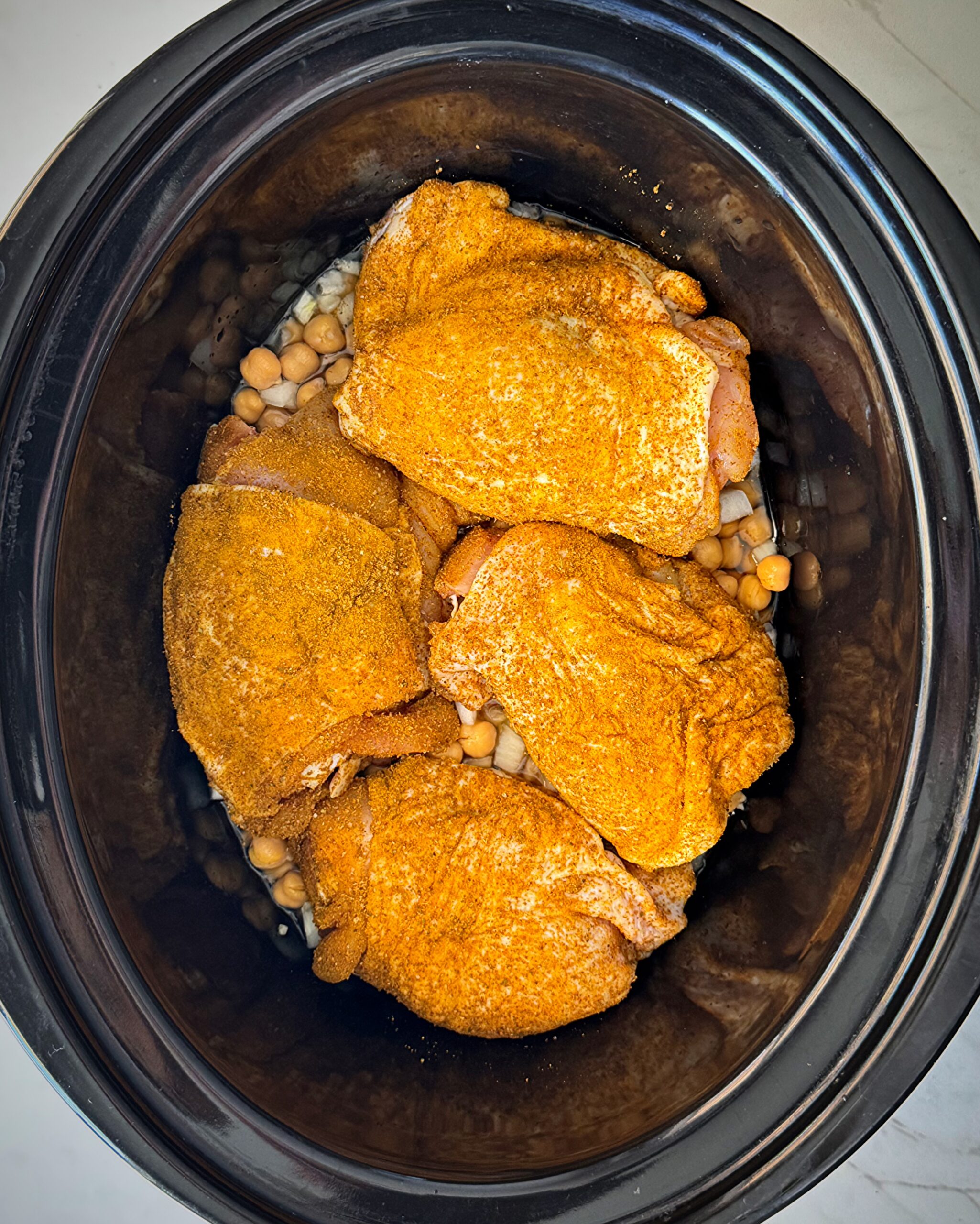 overhead shot of uncooked North African chicken in a black slow cooker