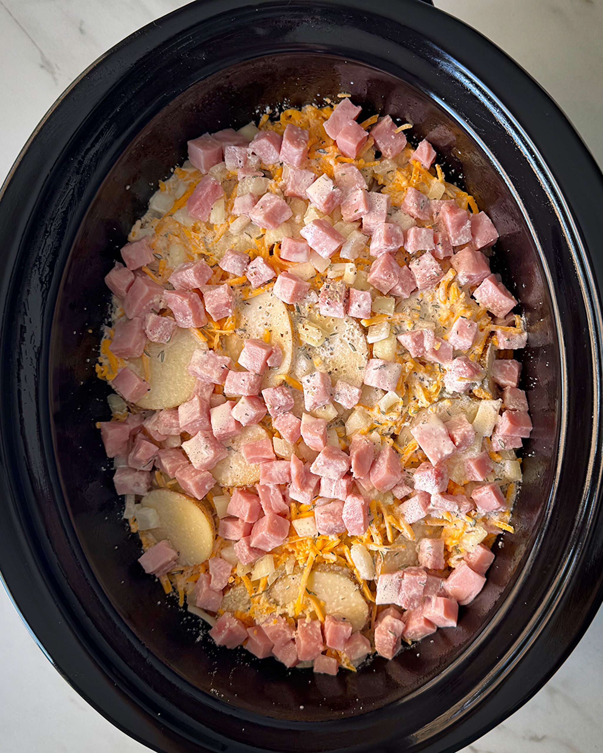 overhead shot of uncooked Scalloped Potatoes and Ham in a black slow cooker