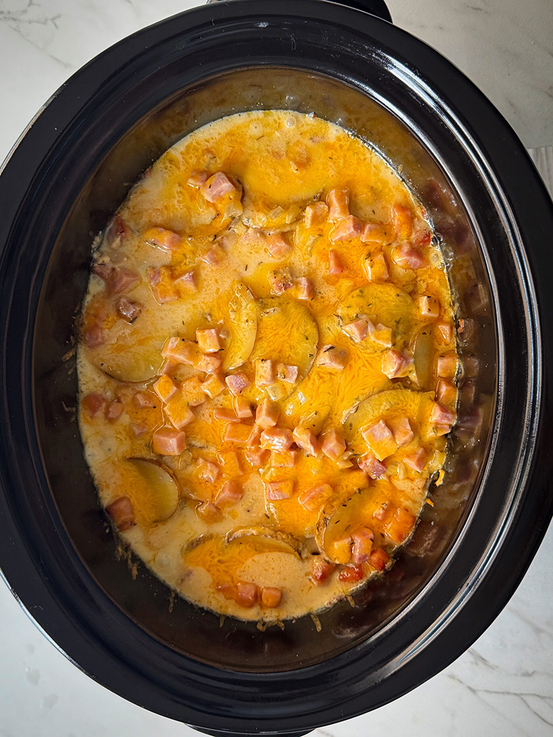 overhead shot of cooked Scalloped Potatoes and Ham in a black slow cooker