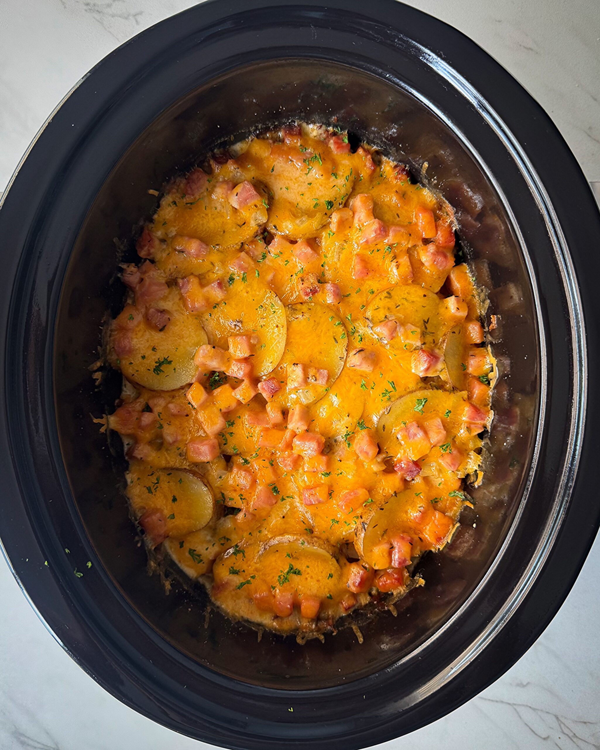 overhead shot of cooked Scalloped Potatoes and Ham in a black slow cooker