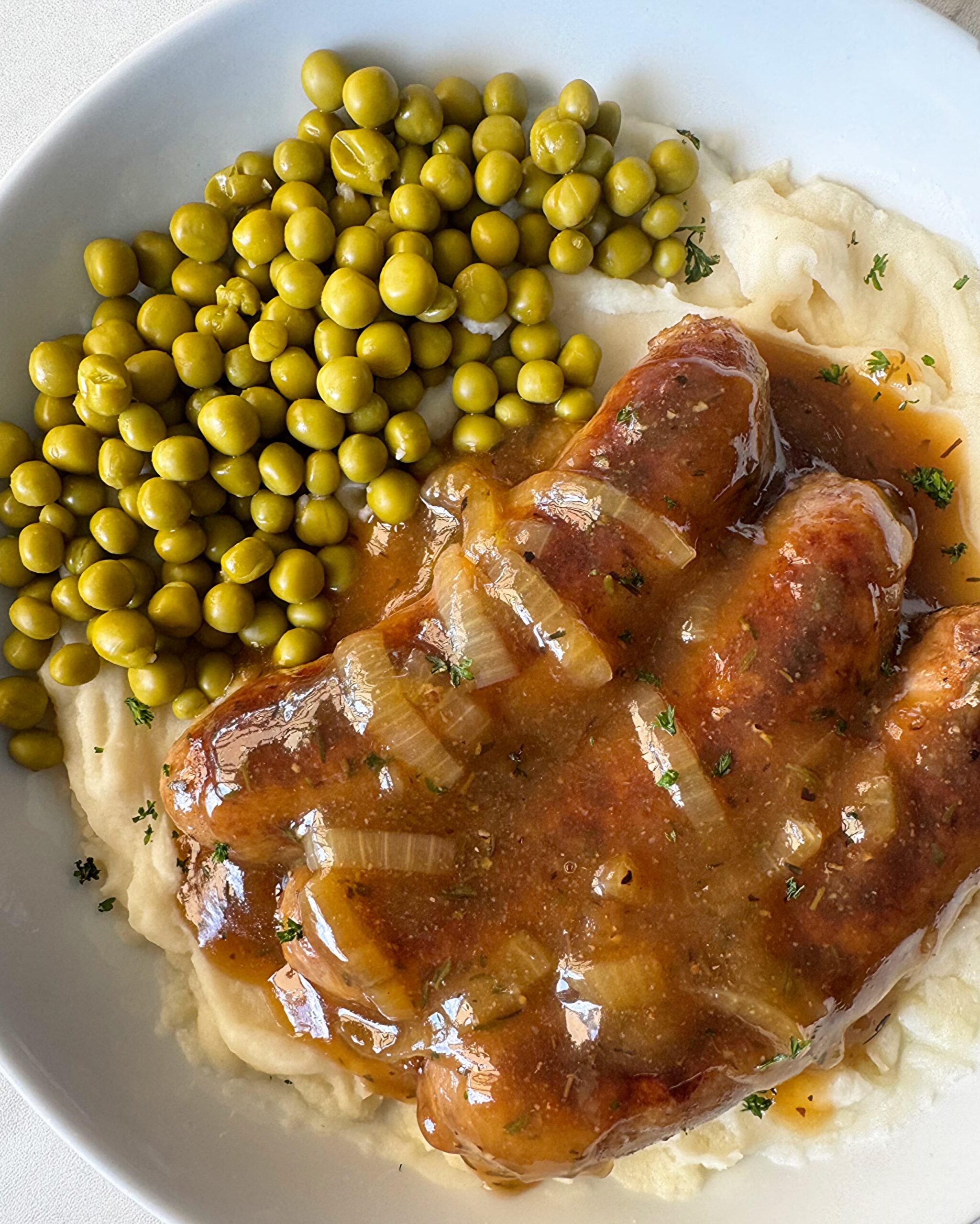 overhead shot of overhead shot of cooked bangers served over mashed potatoes with peas