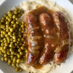 overhead shot of overhead shot of cooked bangers served over mashed potatoes with peas
