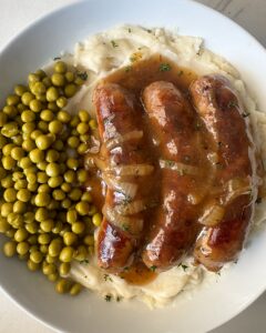 overhead shot of overhead shot of cooked bangers served over mashed potatoes with peas