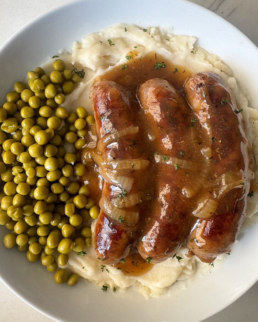overhead shot of overhead shot of cooked bangers served over mashed potatoes with peas