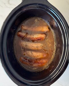 overhead shot of cooked bangers & mash in a black slow cooker