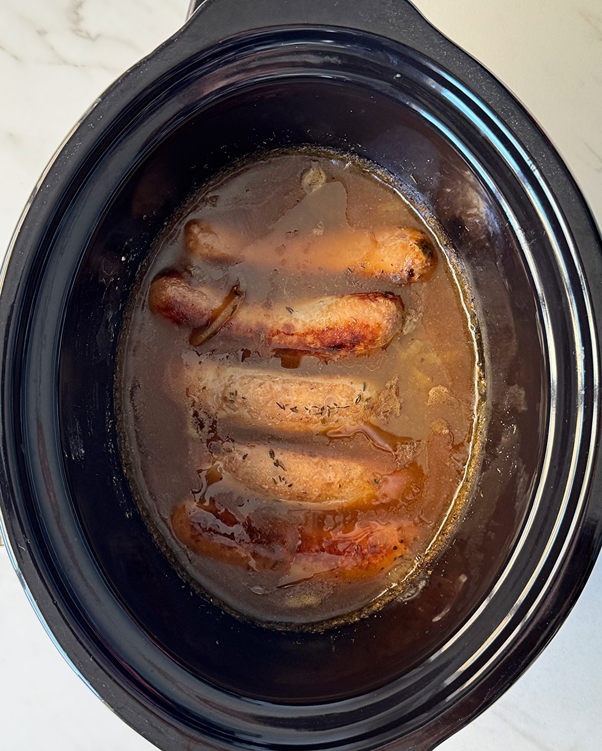overhead shot of cooked bangers & mash in a black slow cooker