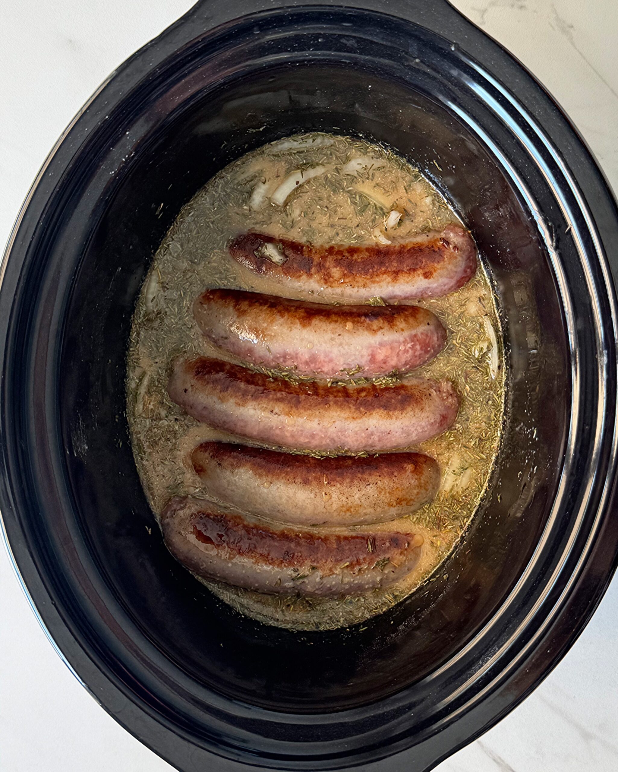 overhead shot of uncooked bangers & mash in a black slow cooker