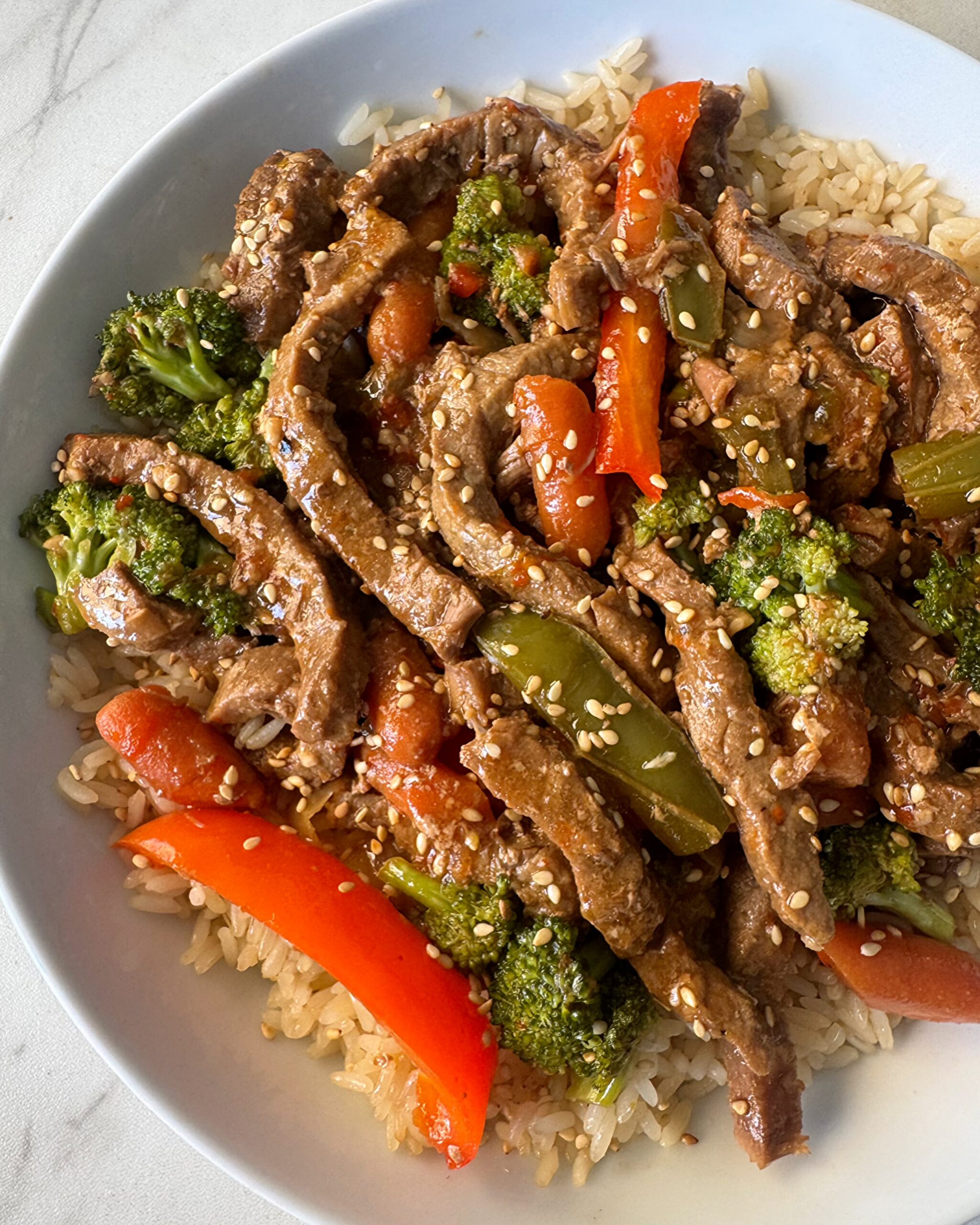 overhead shot of slow cooker beef stir-fry served over rice on a white plate