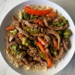 overhead shot of slow cooker beef stir-fry served over rice on a white plate