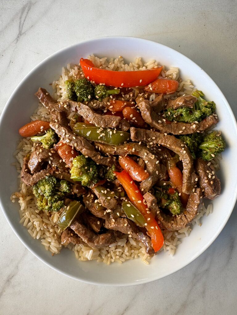 overhead shot of slow cooker beef stir-fry served over rice on a white plate