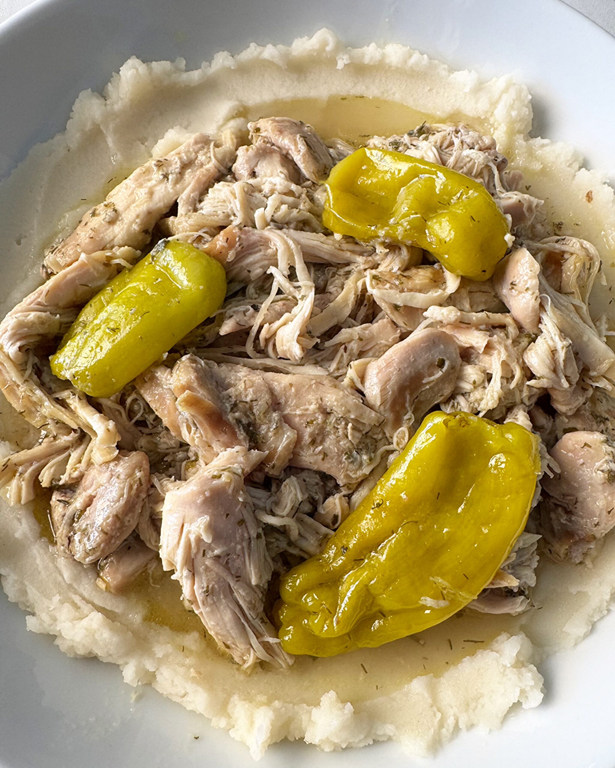 overhead shot of cooked Mississippi Chicken served over mashed potatoes on a white plate