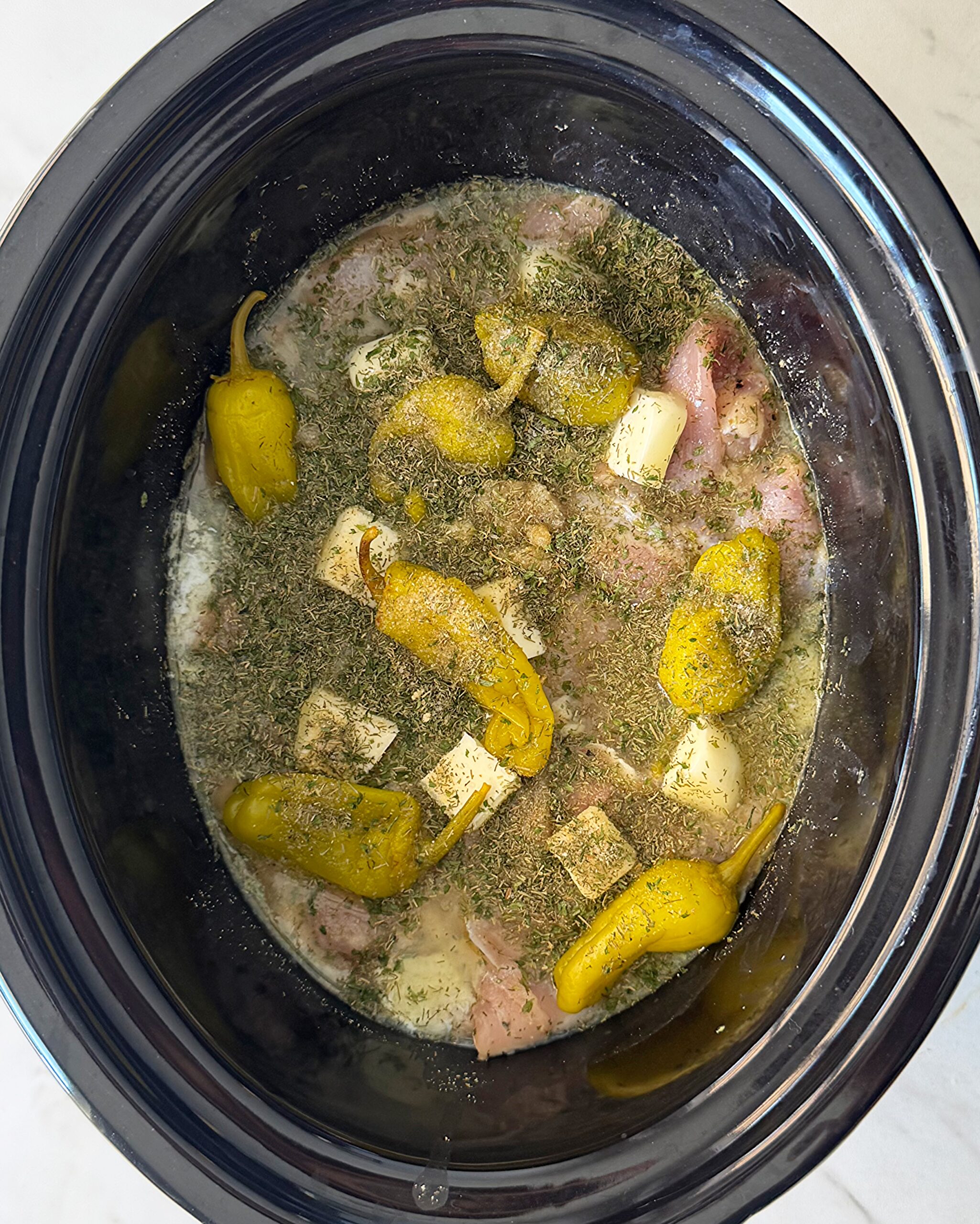 overhead shot of uncooked Mississippi Chicken in a black slow cooker