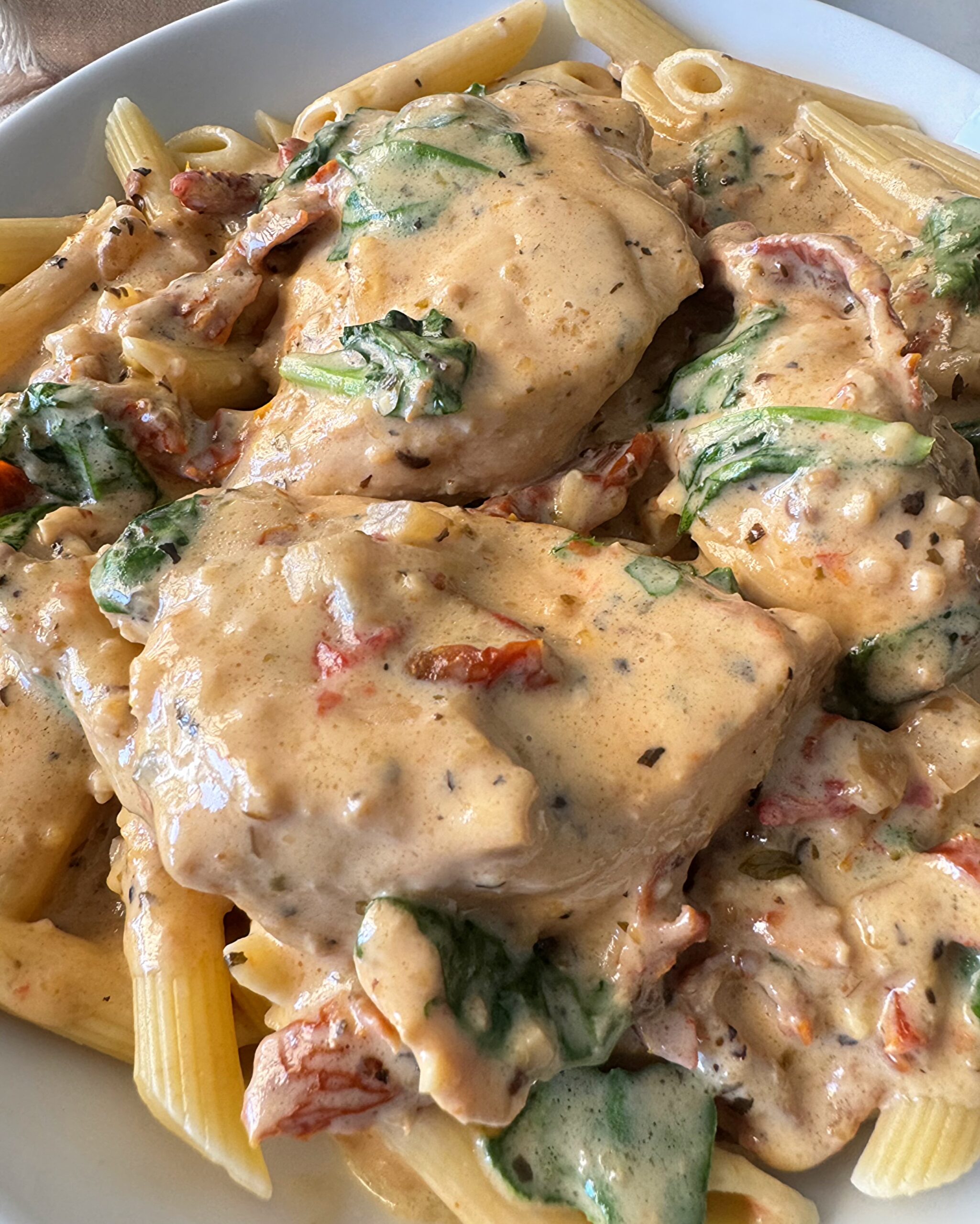 close up shot of Tuscan chicken on a white plate served over penne pasta
