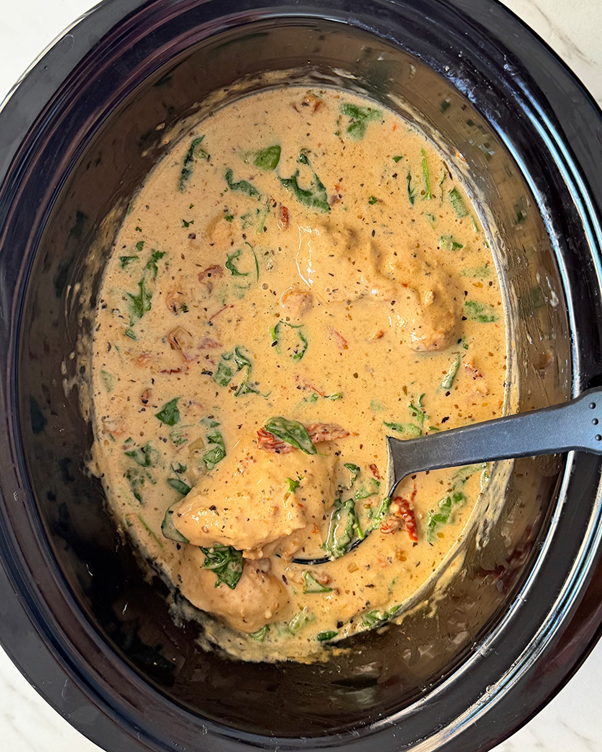 overhead shot of cooked Tuscan chicken in a black slow cooker