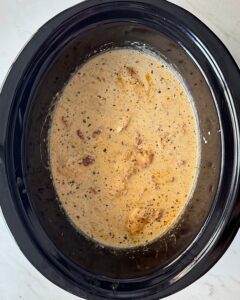 overhead shot of cooked Tuscan chicken in a black slow cooker with cream added
